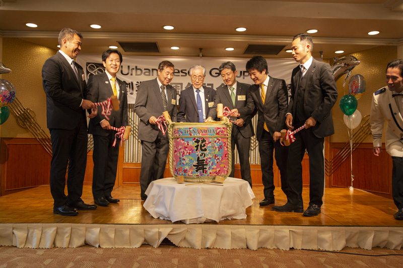 「Urban Resort Group 創業80周年」と記された幕の前で、酒樽の鏡開きに臨む7人