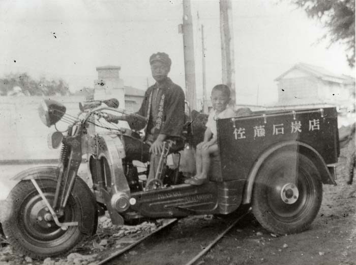 荷台に「佐藤石炭店」と記された三輪トラックと、運転席に座る男性・荷台の子ども